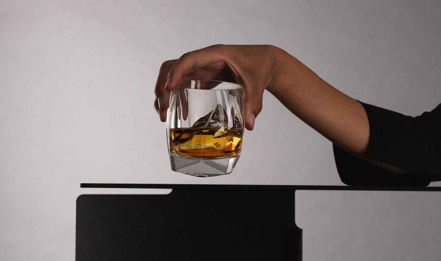 Female hand lifting the clear Rauk Heavy Tumbler by the mouth rim, highlighting the weight of the glass and showing its thick bottomed base. 