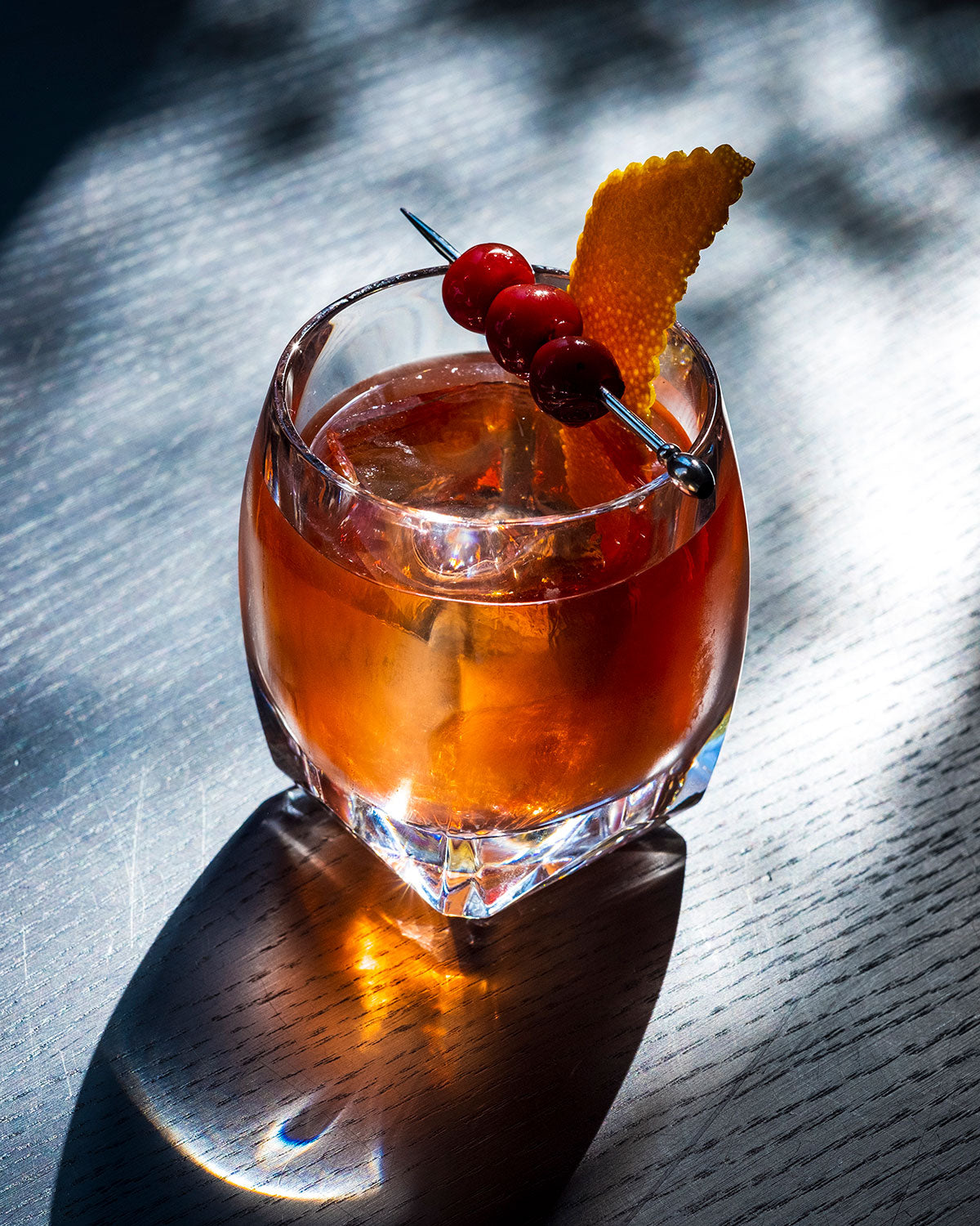 A bright red Godfather cocktail served in our clear Heavy Tumbler glass with cherry and orange peel garnish.