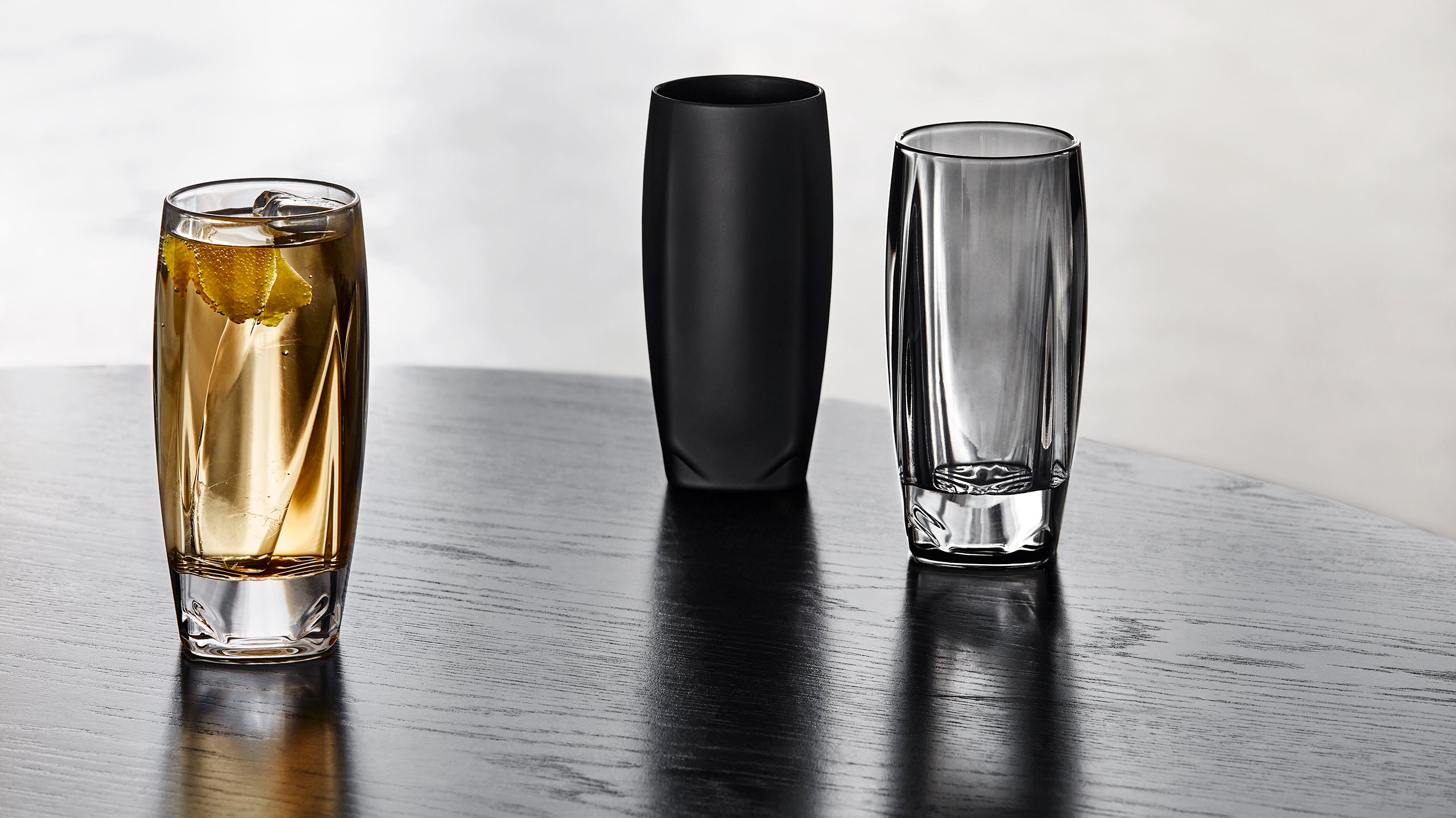 Our range of Vawe Highball Glasses in clear, black, and grey shown standing on a table.