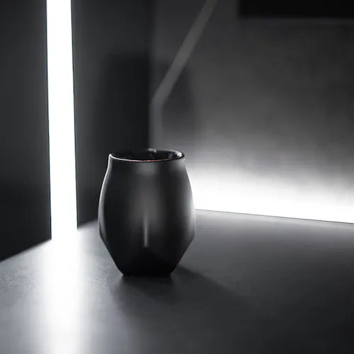 A image of the norlan whisky glass vaild (black) edition in a futuristic minimalist setting with a an angular back drop of a vertical led bar that gives it a space like setting.