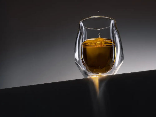 The Norlan Whisky Glass Clear placed on the edge of a black ledge against an illuminated background.