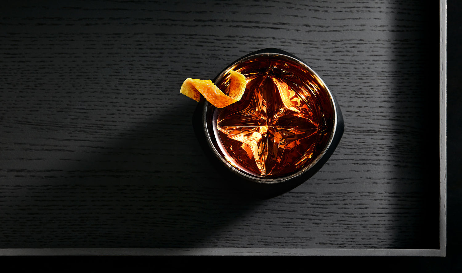 Enhance your whiskey with the Vaild black edition of the Rauk Heavy Tumbler is shown from above. A whisky-based cocktail served up with an orange peel garnish helps show how the fluid inside sparkles when light is reflected within. 