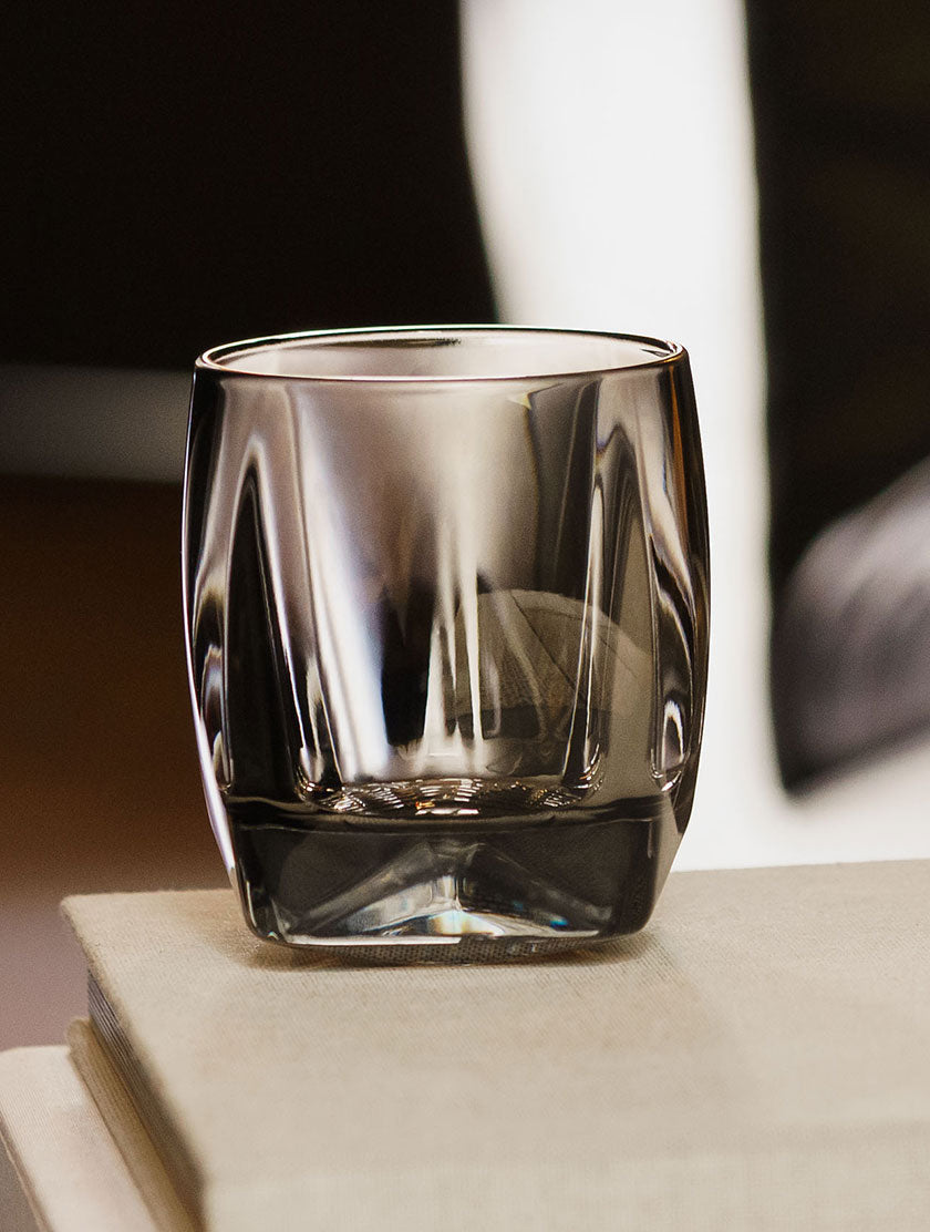 Color your whisky with the sinder grey Rauk Heavy Tumbler, shown here on top of some white books with a leather lounge chair in the background. 
