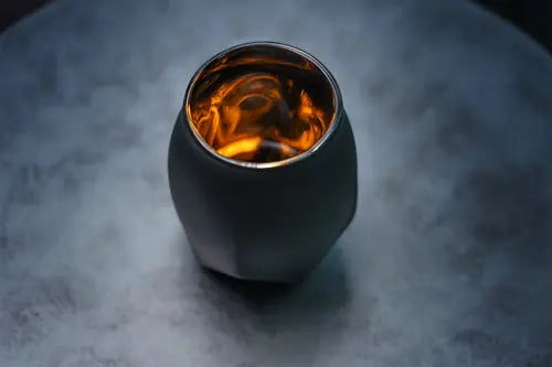 Semi-arial view of the Norlan Whisky Glass Vaild (Black) sitting on a stone tabletop showing a glimpse of how whiskey's golden hue is amplified in the glass.