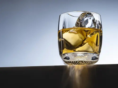 A lifestyle image of the Rauk Heavy Tumbler 250 mL (Clear) sitting on a black ledge against a light blue background. 