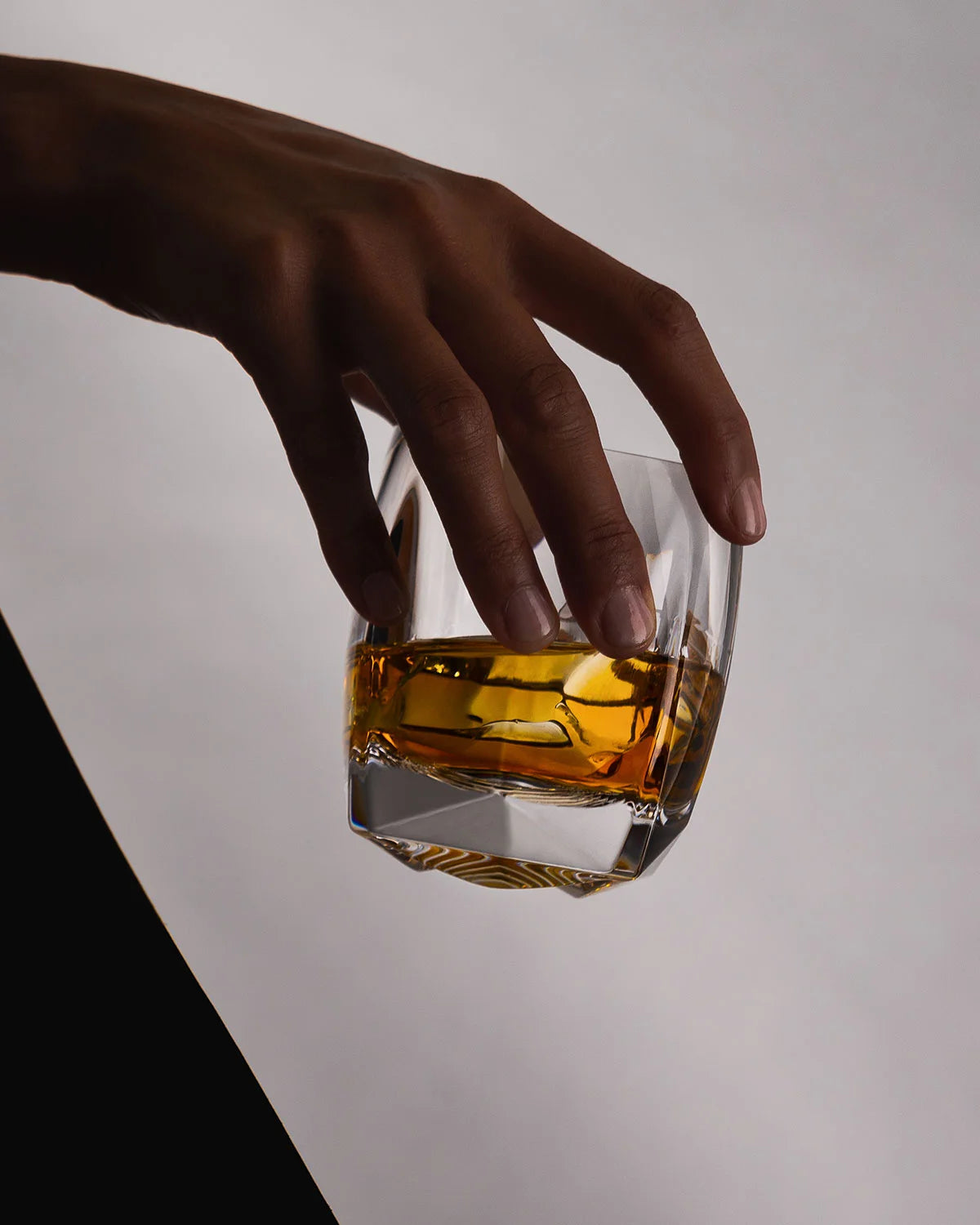 Clear Rauk Heavy Tumbler held by female hand, showing faceted texture and weighty three-dimensional base, ideal for bourbon or whiskey