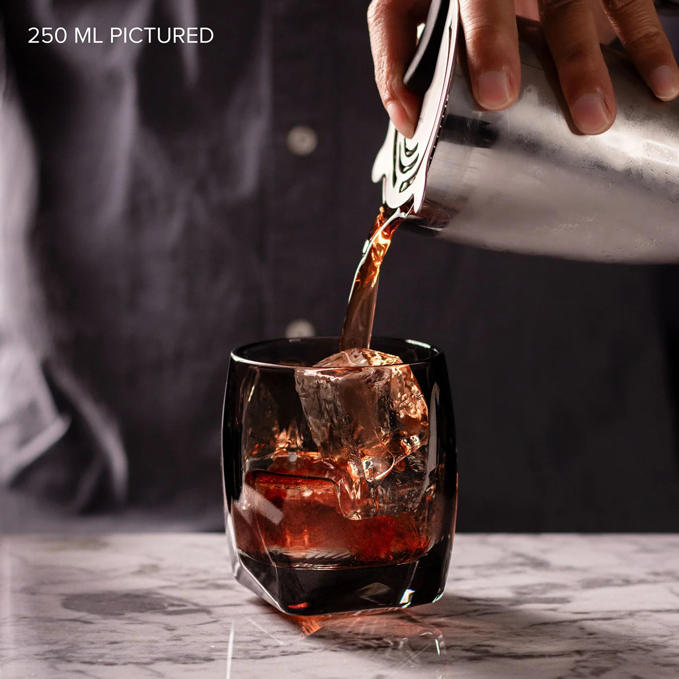 A bourbon-based Boulevardier cocktail being poured over ice into a smoky gray non-leaded crystal tumbler