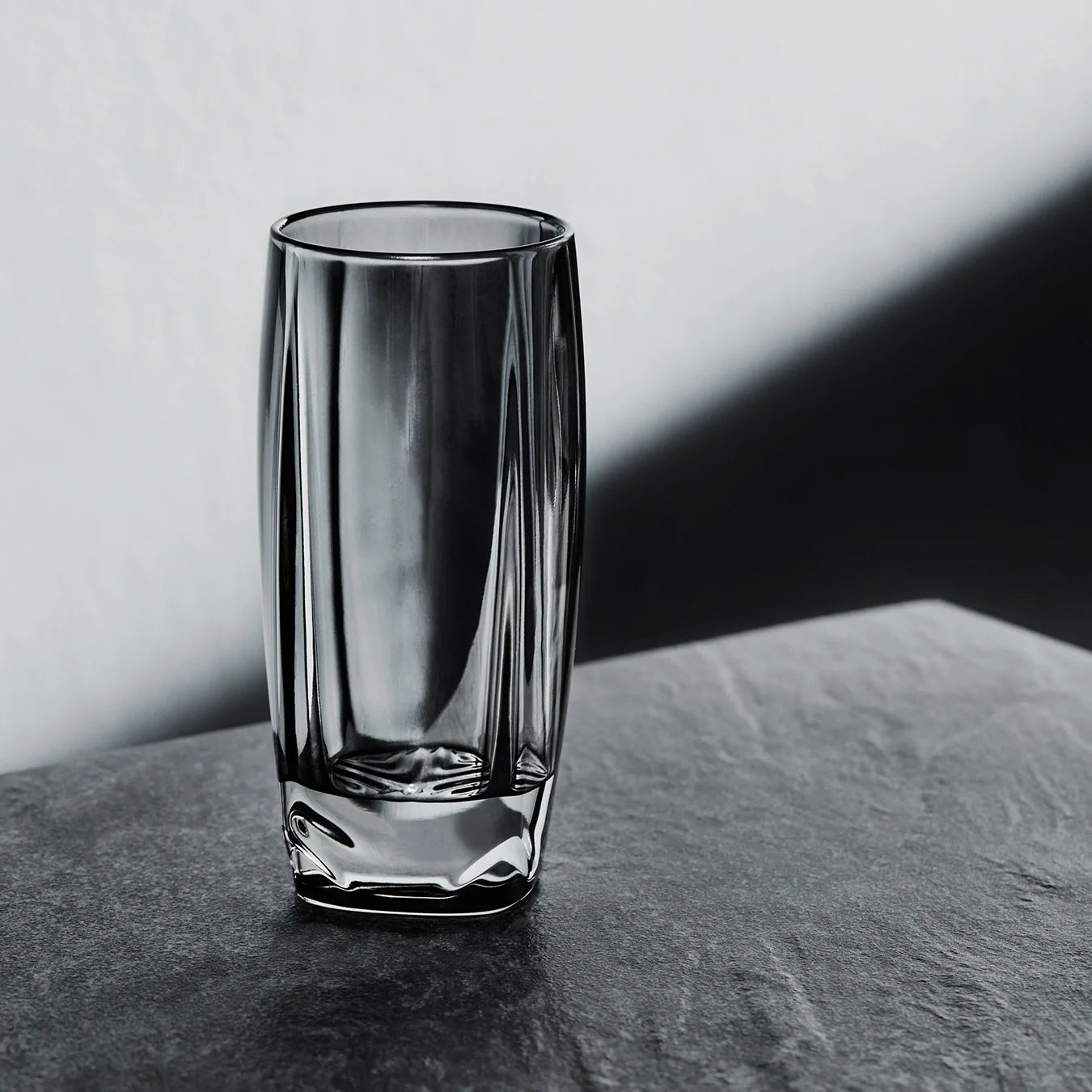 An elegant non-leaded crystal highball glass with rounded form and chevron shaped design detail at thick base. 