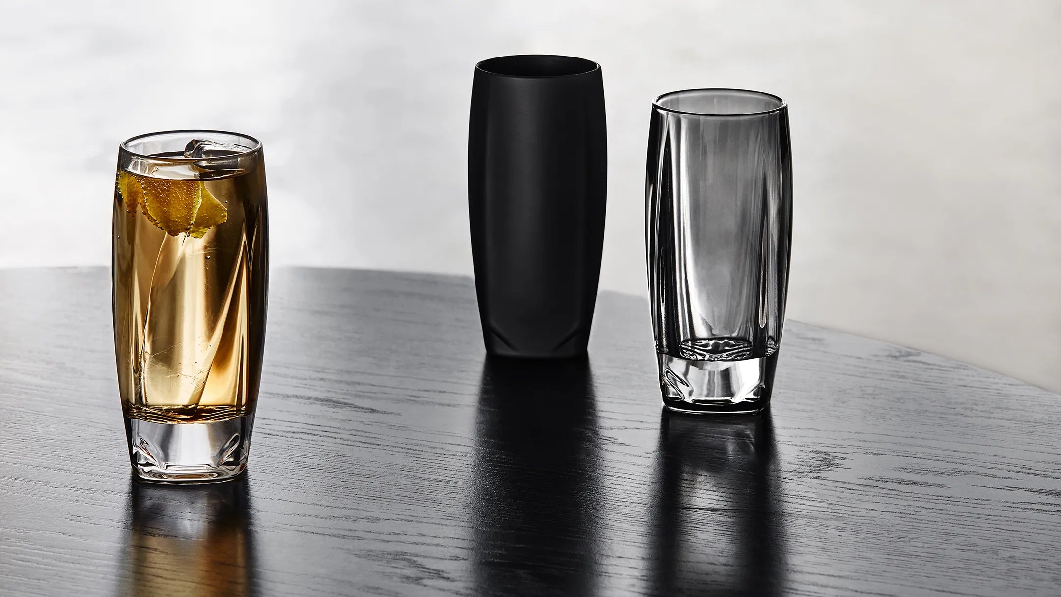 Our range of Vawe Highball Glasses for whiskey and soda drinks, shown in clear, black, and grey shown standing on a table.