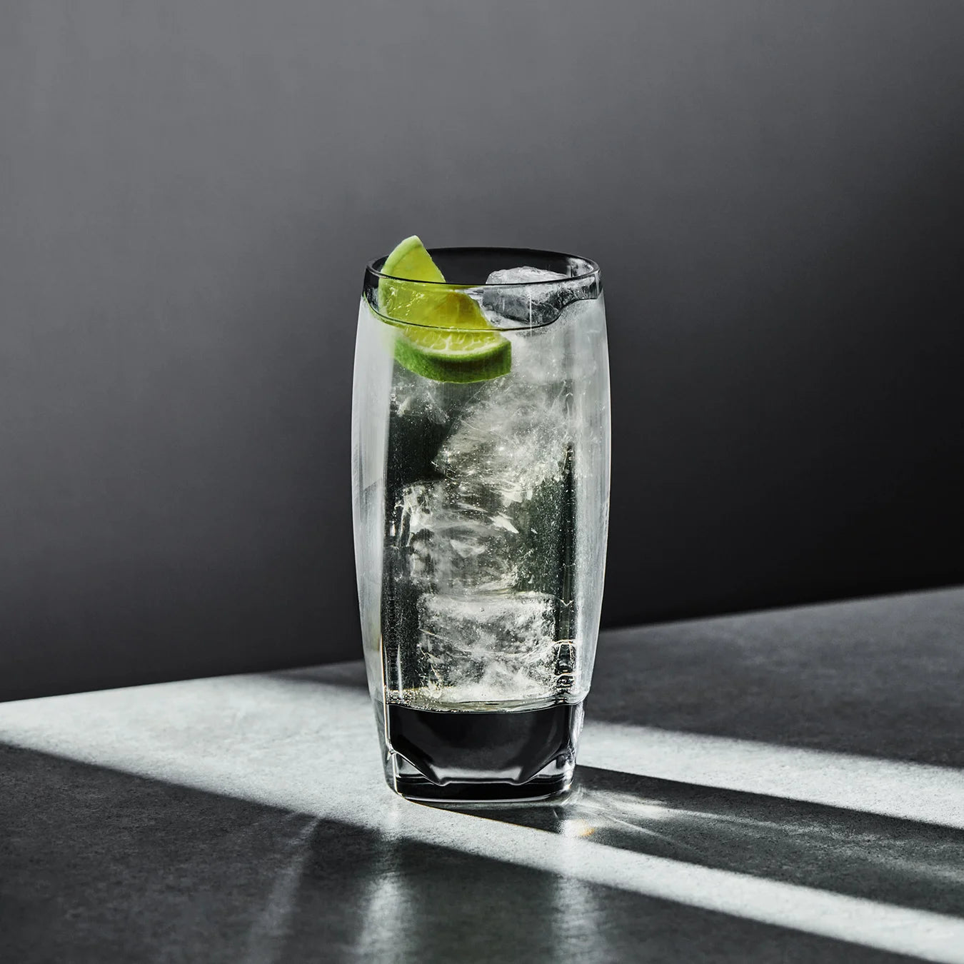 A smoke-grey Vawe Highball Glass in non-leaded crystal featuring a whiskey dry and lime cocktail